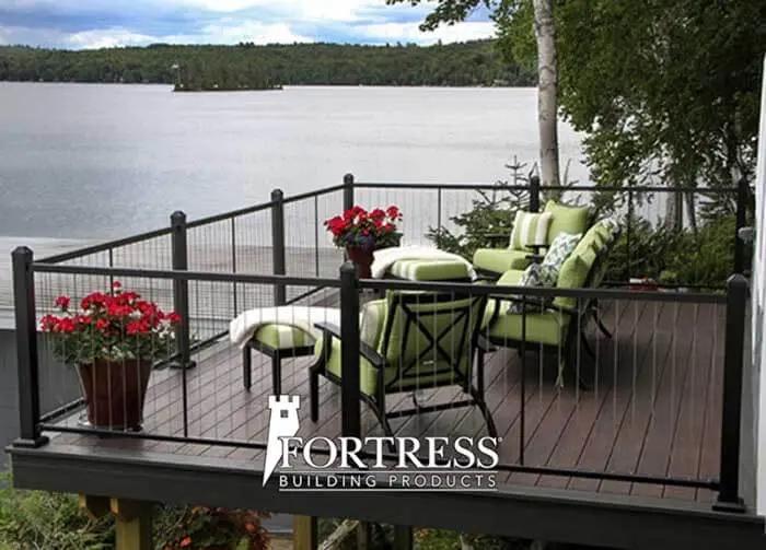 Deck with padded outdoor furniture on the lakeside with trees and flowers.