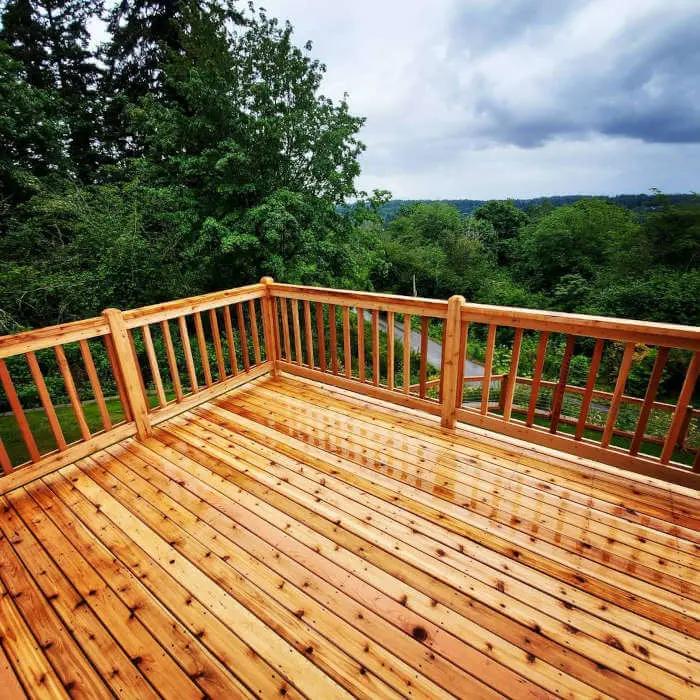 Natural cedar wood deck with cedar railing and a cedar frame wire fence in a forested area surrounded by trees.