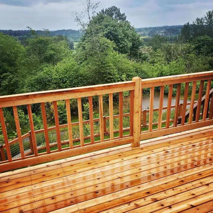 Natural cedar railing on a natural cedar deck in a forested area surrounded by trees.